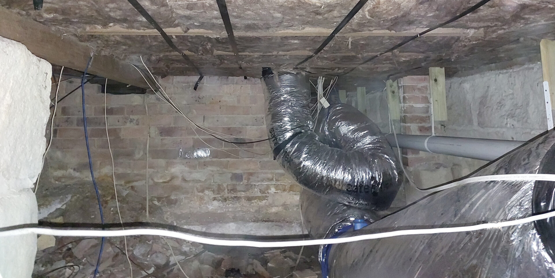 Underfloor insulation work area with exposed brick and ductwork