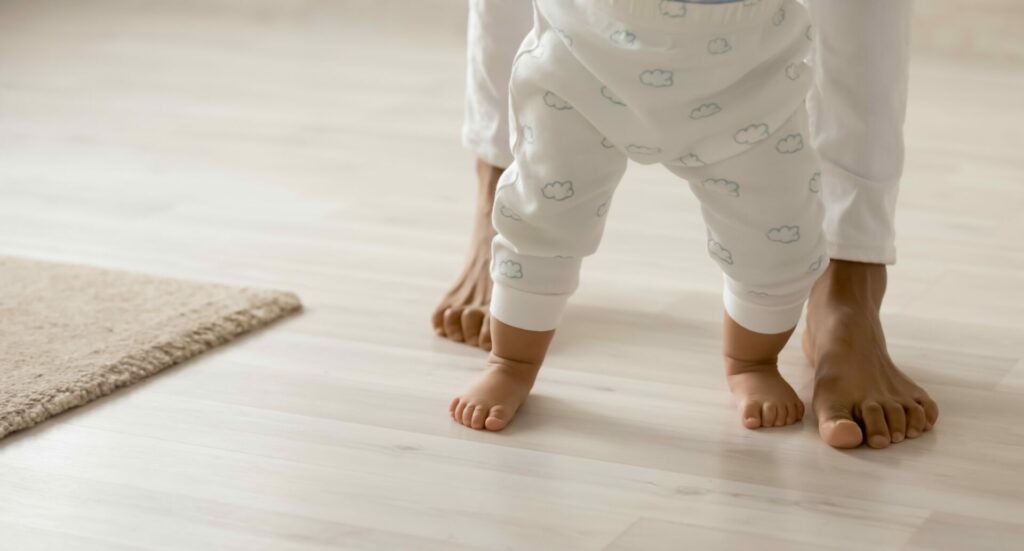 A mother helps her toddler walk on the insulated, sustainable floors in their home.