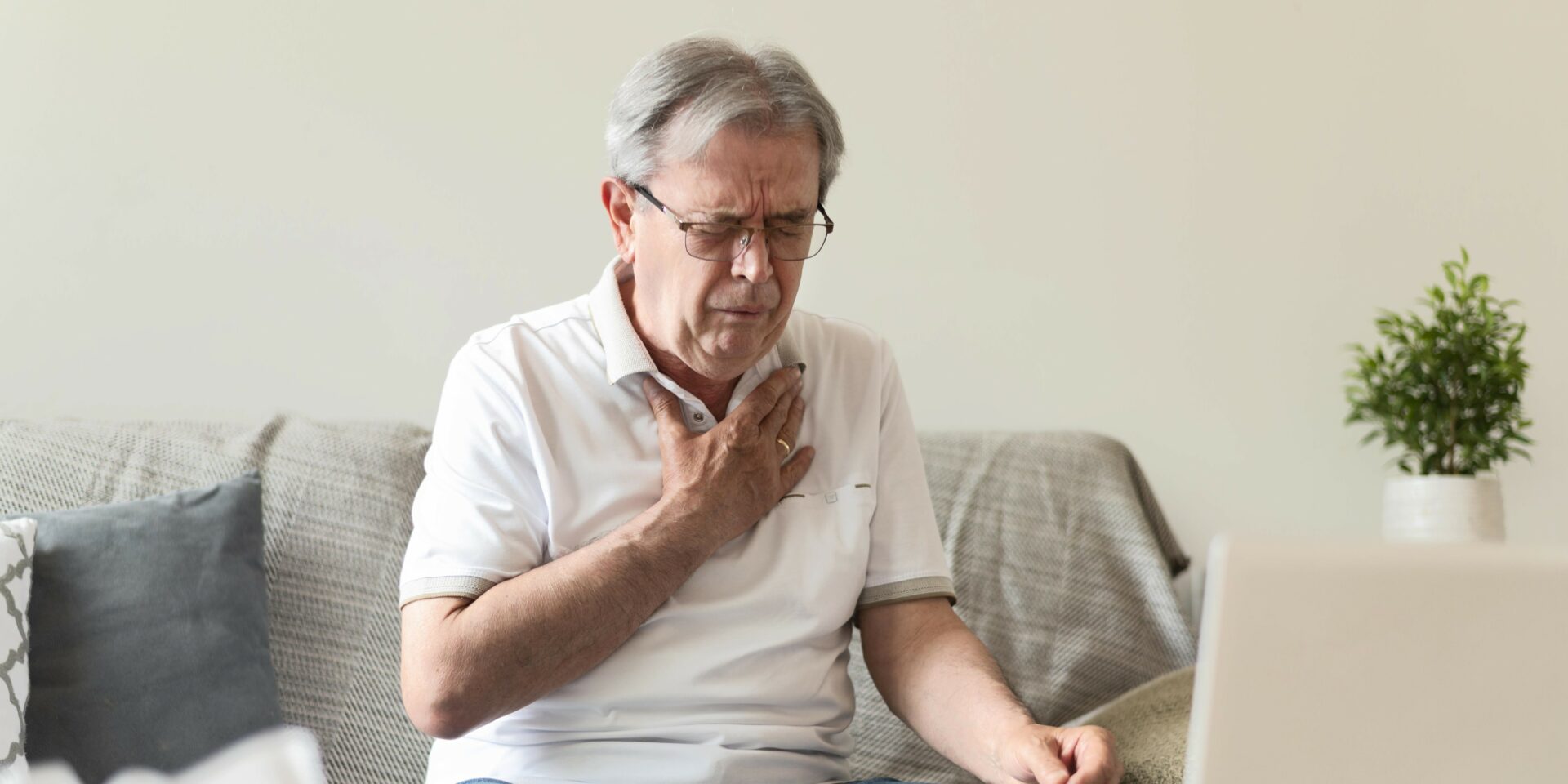 An elderly man sits on his couch experiencing chest pain after being exposed to asbestos insulation in Australia.