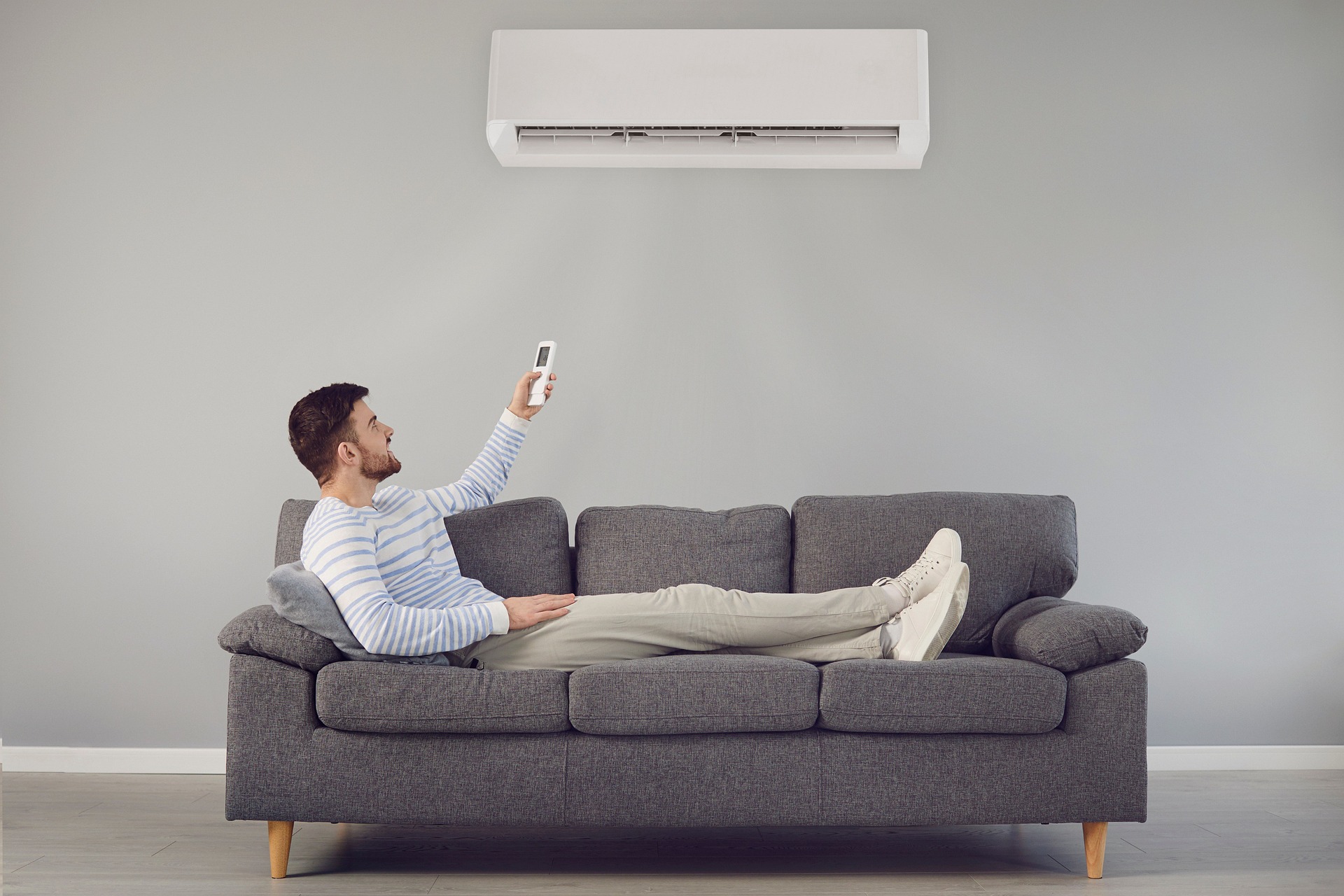 Man sits on a couch controlling the air conditioner in his home.